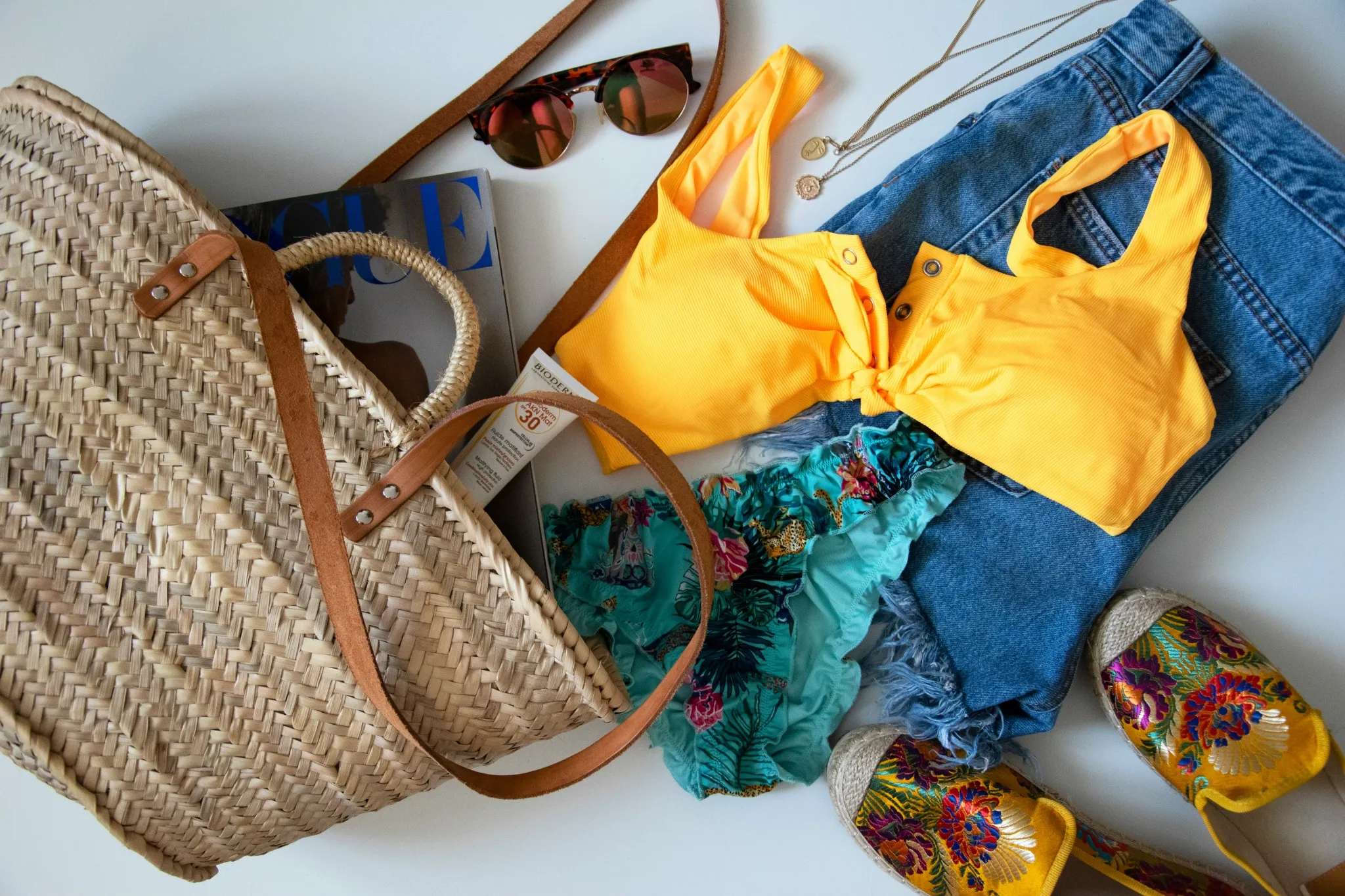 Flat lay of tropical travel essentials including swimsuit, sunscreen, sandals, and denim shorts for a Bali vacation packing list.